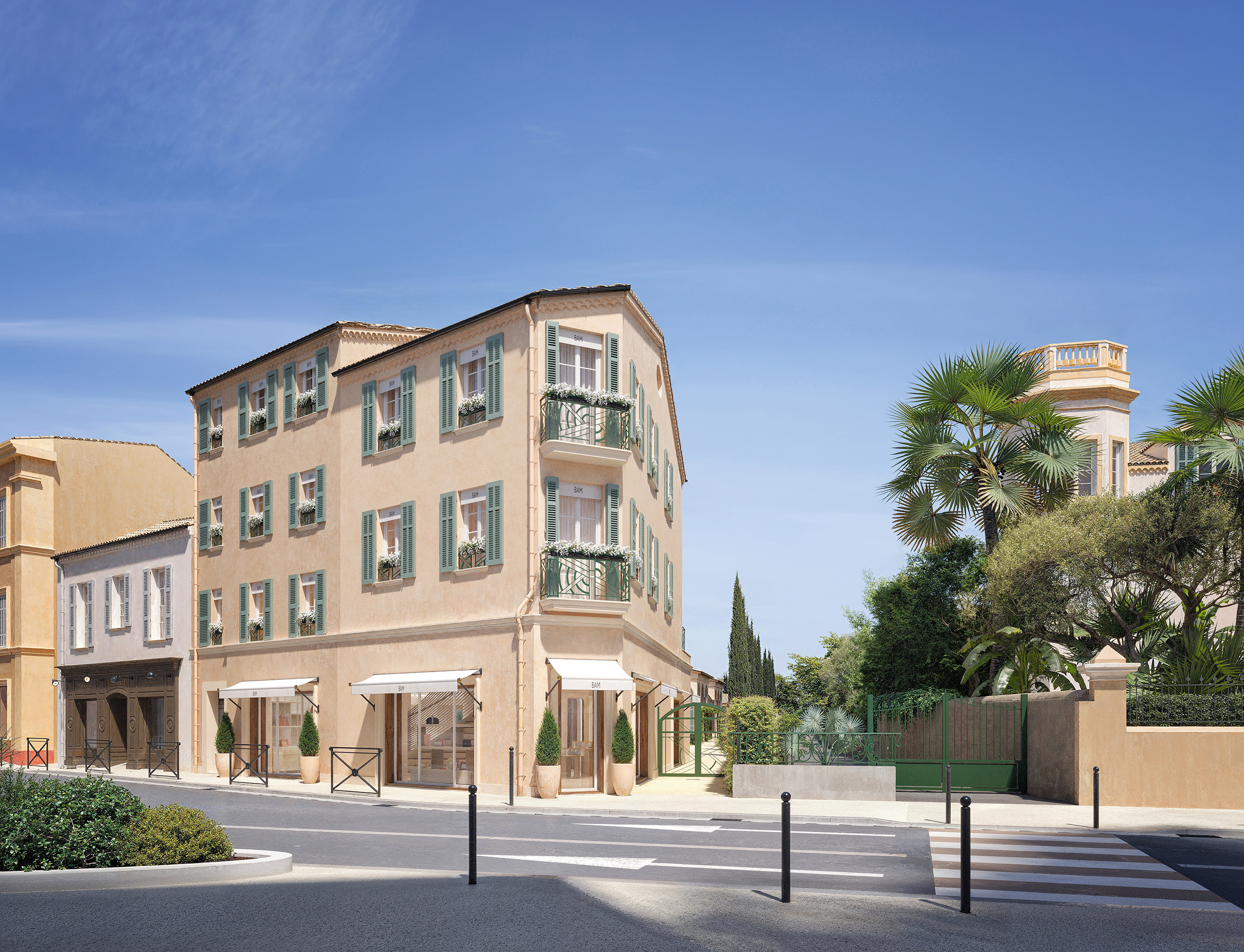 Façade sur rue de la boutique de luxe à Saint-Tropez – bâtiment provençal en enduit ocre, persiennes vert sauge, auvents blancs et enseigne