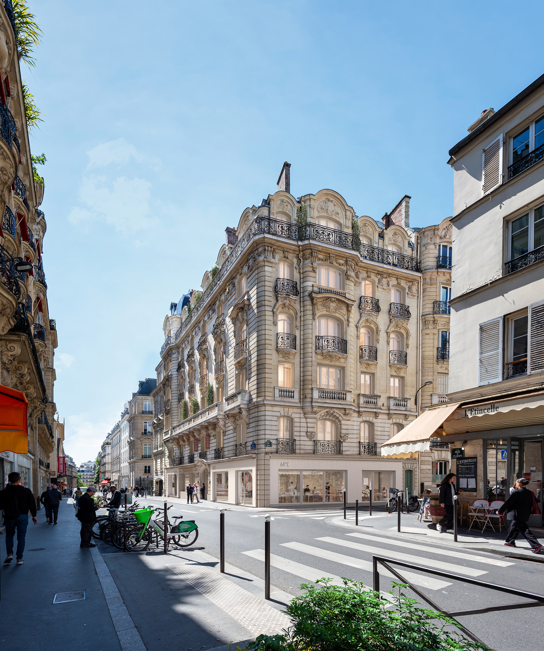 29 Clichy – immeuble haussmannien en pierre de taille à l'angle d'une rue parisienne animée, rez-de-chaussée vitré, ciel bleu.