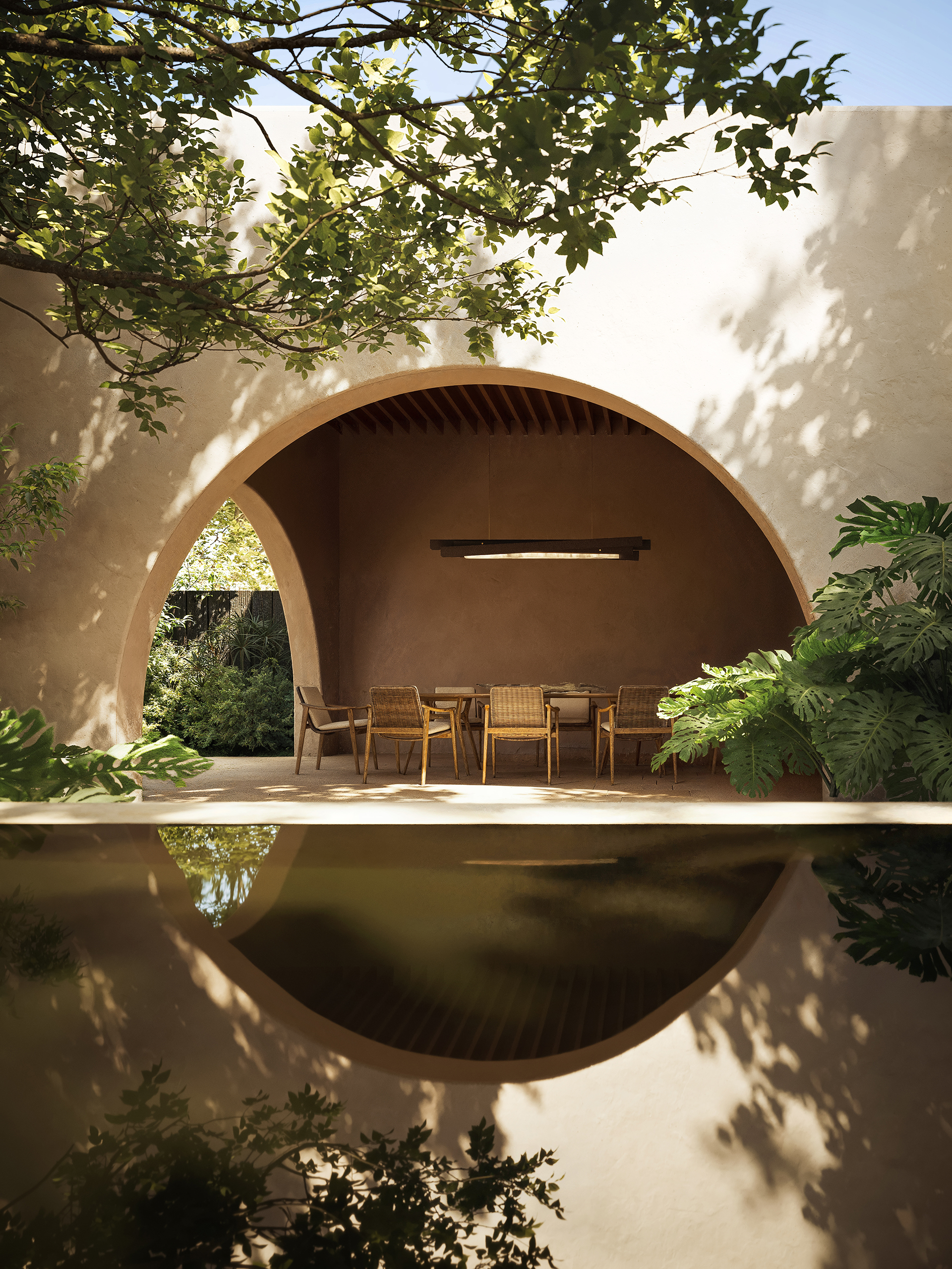 Espace repas extérieur Incandescence Hacienda – arche circulaire en stuc terracotta, plafond en bois brûlé, suspension en albâtre et bassin réfléchissant.