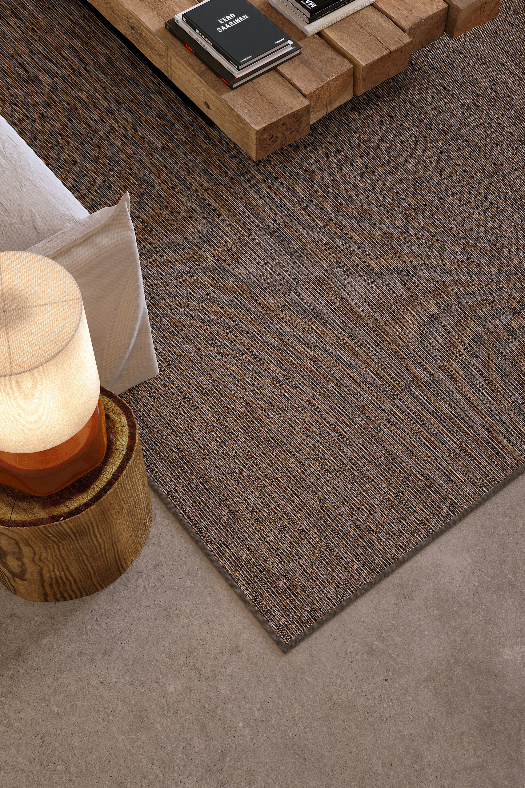 Moquette Jakarta Balsan en camaïeu brun rayé fin, mise en scène sur béton ciré avec table en billes de bois et lampe céramique ambre